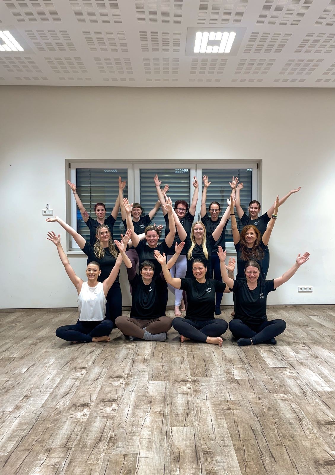 Team-Gruppenfoto nach einem Firmen-Yoga-Workshop, alle mit erhobenen Armen und einheitlichen Shirts